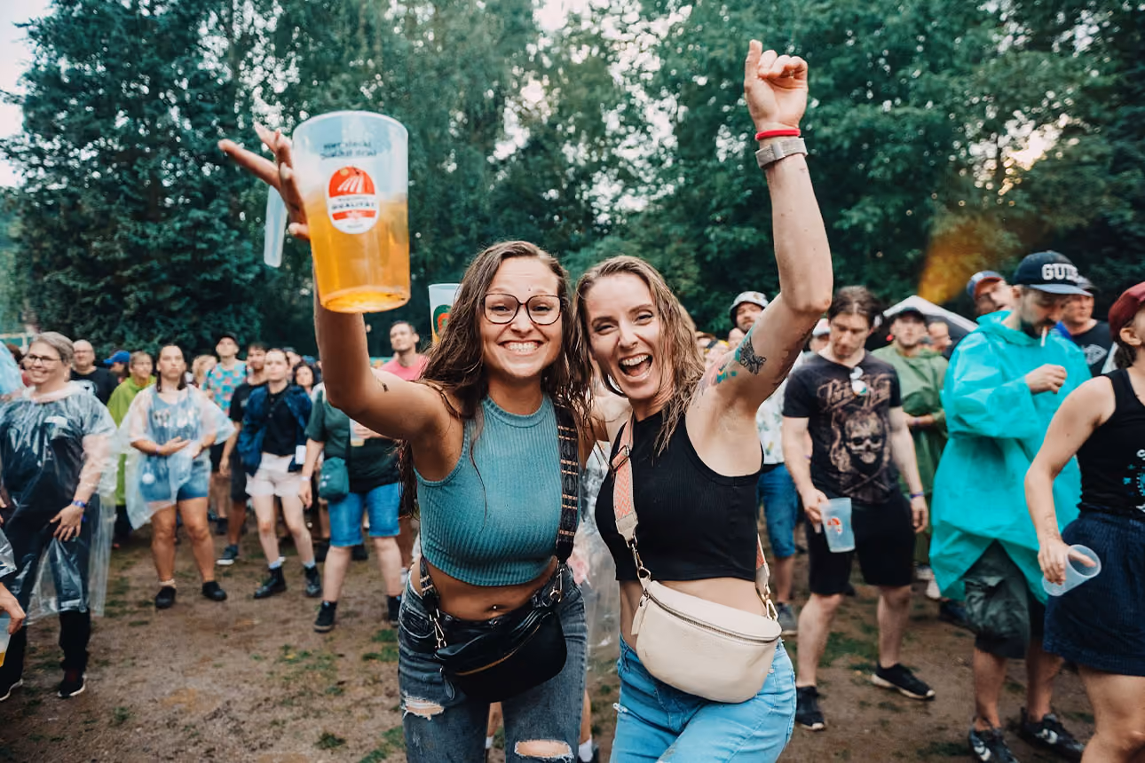 Zwei Frauen halten die Arme in die Luft und freuen sich. Die Linke Person hält ein Bier in der Hand.